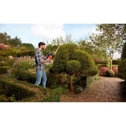 BLACKDECKER BEHTS401 hedge trimmer used in garden landscaping, orange and black design, outdoor setting