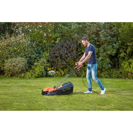 BLACK+DECKER BEMW451BH electric lawn mower in use on green grass in a garden setting.