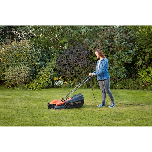 BLACKDECKER BEMW451 electric lawn mower in use on grass by a person, orange and black design, side angle.