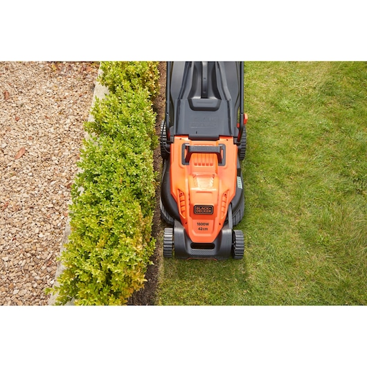 BLACKDECKER BEMW481BH electric lawn mower top view in use, orange and black design cutting grass near hedge.