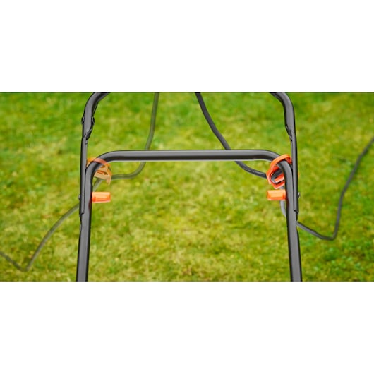 BLACKDECKER BEMW481ES lawn mower handle close-up with orange lever clips on green grass background.