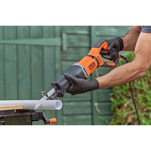 BLACK+DECKER BES301 reciprocating saw cutting white plastic pipe, outdoor usage shown.