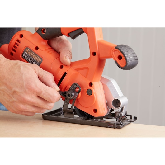 Photo of BLACK+DECKER BES510K compact circular saw, orange and black, being adjusted by hand on a wood surface.