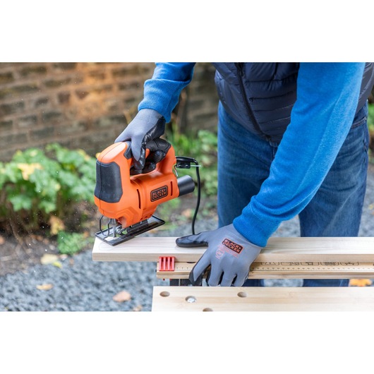 Photo of BLACKDECKER BES602 jigsaw in use, cutting wood, operator wearing gloves, outdoor setting.