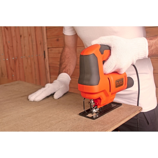 Photo of BLACKDECKER BES603 jigsaw in use cutting wood, viewed from the side, user wearing white gloves.