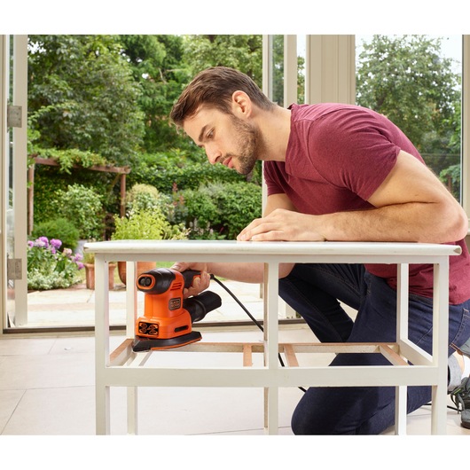 BLACKDECKER BEW200K sander in use on white table, indoor workshop setting, product photography.