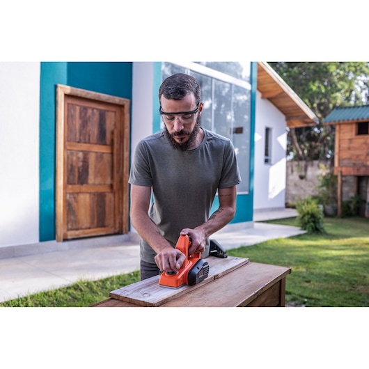 Photo of a person using a BLACK+DECKER BEW712 electric planer on a wooden board outdoors.