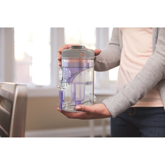 Photo of person holding BLACKDECKER BHFEV182CP vacuum dust canister with transparent purple components indoors.