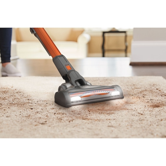 BLACKDECKER BHFEV182C stick vacuum cleaning light-colored carpet with visible dirt in a living room.
