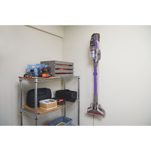 BLACKDECKER BHFEV362DP cordless stick vacuum mounted on wall in utility room beside metal shelving with tools.