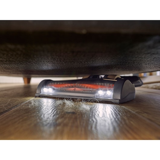 BLACKDECKER BHFEV36B2DW cordless vacuum cleaner head with LED lights cleaning pet hair under furniture, low-angle view.