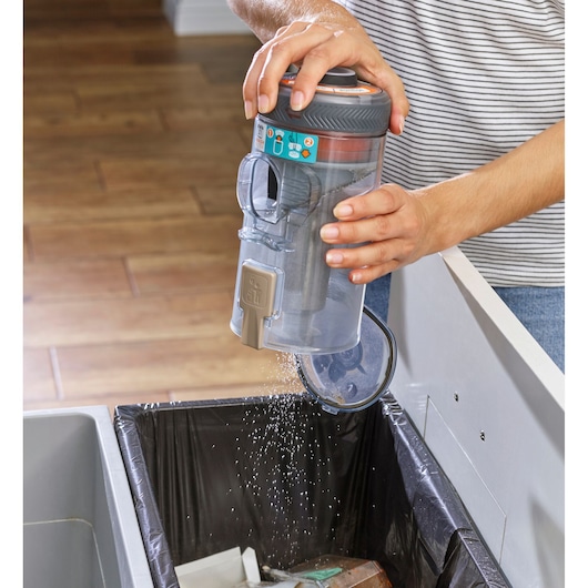BLACKDECKER BHFEV36B2DW vacuum dust canister being emptied into a trash bin, demonstrating easy cleaning.