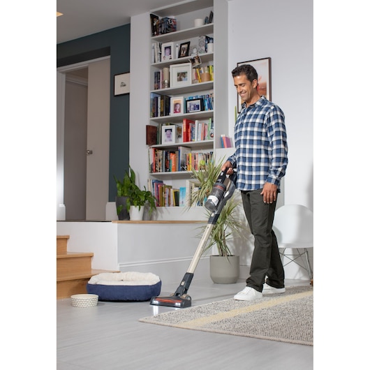 BLACKDECKER BHFEV36B2DW cordless stick vacuum cleaning a living room floor.