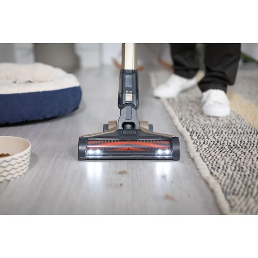 BLACKDECKER BHFEV36B2DW vacuum cleaner head with LED lights cleaning hard floor beside rug.