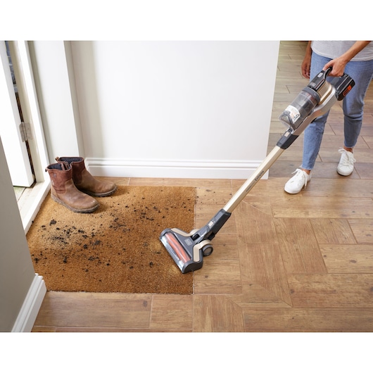 A BLACK+DECKER cordless vacuum cleaner is cleaning scattered debris from a wooden floor.
