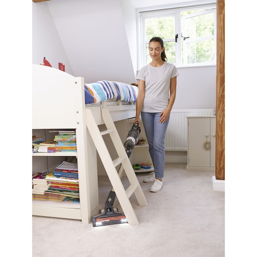 BLACKDECKER BHFEV36B2DW cordless stick vacuum cleaning carpet in a child's bedroom, bookshelf and bed visible.