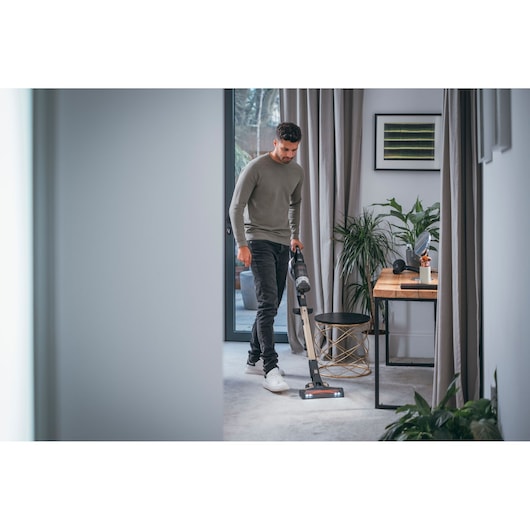BLACKDECKER BHFEV36B2D cordless stick vacuum cleaning carpet in modern living room.