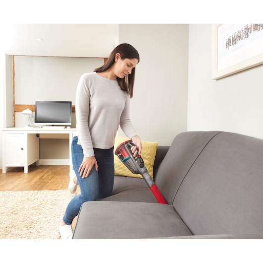 BLACKDECKER BHHV315B handheld vacuum used to clean a gray sofa in a modern living room.