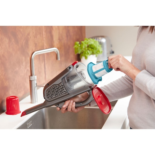 BLACKDECKER BHHV315J handheld vacuum with filter being cleaned in kitchen setting.