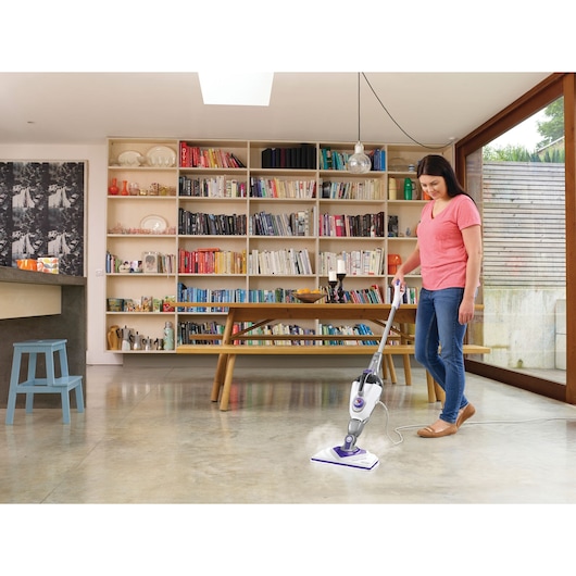 BLACK+DECKER BHSM1615DSM steam mop cleaning a light-colored floor in a modern room with bookshelves.