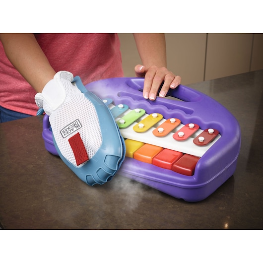 Photo of BLACK+DECKER BHSM1615DSM steam cleaning mitt in use, cleaning a colorful toy xylophone on a table.