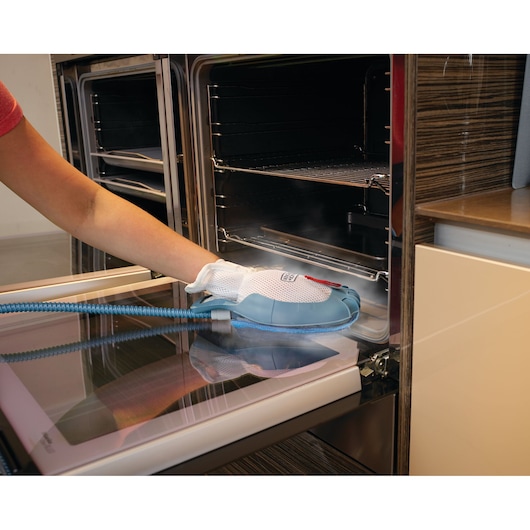 BLACKDECKER BHSM166DSM steam cleaning glove cleaning oven door in kitchen, close-up side angle.