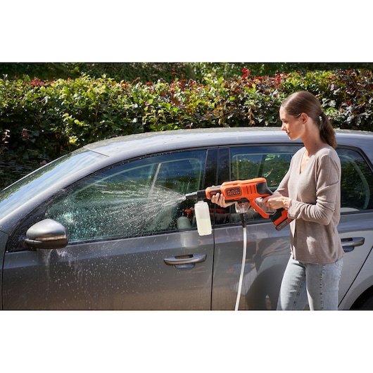BLACKDECKER BZOSBSK3 cordless pressure washer spraying water and soap on a car in outdoor setting.