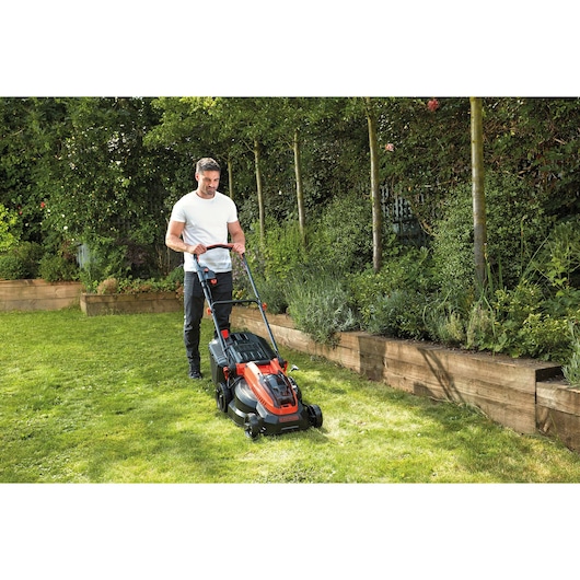 BLACKDECKER CLM3825L2 lawn mower in use on garden grass near wooden planters.