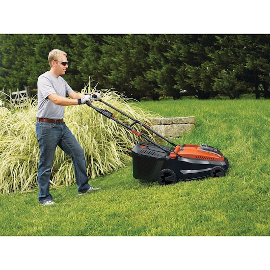 BLACKDECKER CLM3825L2 lawn mower in use on grass, side view, orange and black design, outdoor setting.