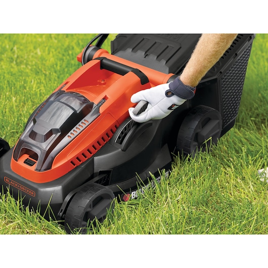 BLACKDECKER CLM3825L2 lawn mower close-up, orange and black design, gloved hand adjusting height on grass.