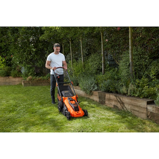 BLACKDECKER CLMA4825L2 lawn mower in use on grass near a garden bed, orange and black design.