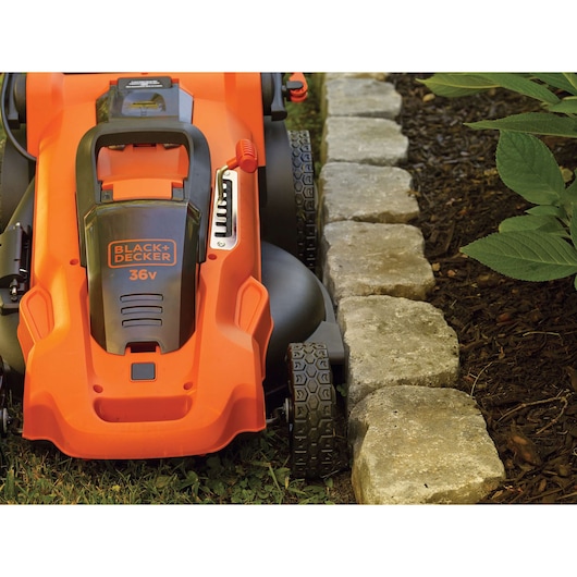 Photo of BLACKDECKER CLMA4825L2 lawn mower close-up mowing near stone edge, orange body, 36V branding visible.