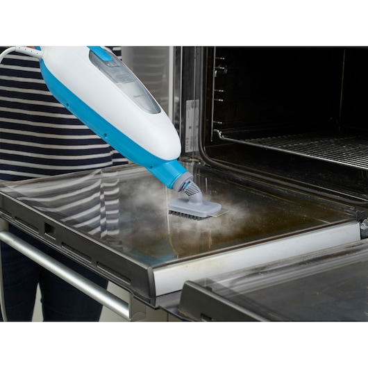 BLACKDECKER FSMH13E10 steam cleaner cleaning oven door, side angle, blue and white handheld device.