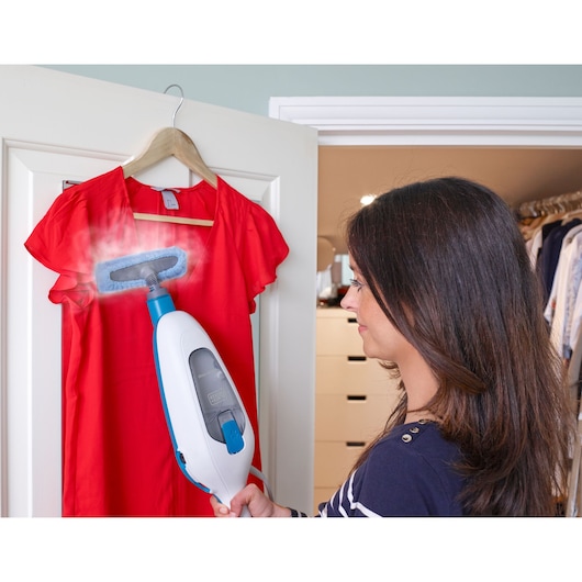 BLACKDECKER FSMH13E10 handheld steam cleaner used to freshen a red dress on a hanger in a closet setting.