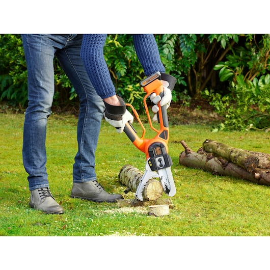 BLACKDECKER GKC1000L cordless chainsaw cutting log outdoors, person wearing gloves.