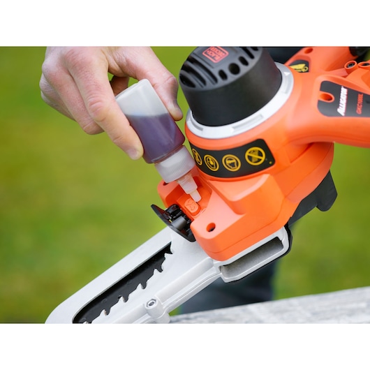 BLACKDECKER GKC1000L chainsaw being oiled, close-up of blade and oil bottle outdoors.