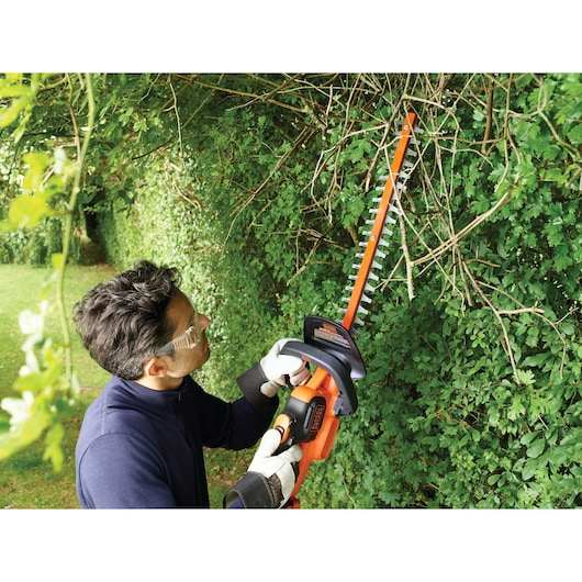 BLACKDECKER GTC18504PC hedge trimmer in use on green shrubs outdoors.