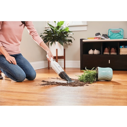 BLACKDECKER HLVC315B11 handheld vacuum cleaning soil from spilled plant on hardwood floor, indoor scene.