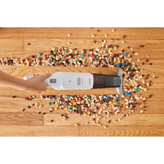 BLACK+DECKER HLVC315B11 handheld vacuum cleaning mixed dry snacks from hardwood floor, top view.