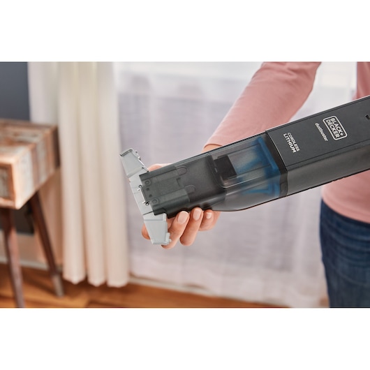 Photo of BLACKDECKER HLVC320J11 cordless handheld vacuum being held, focusing on dustbin removal.