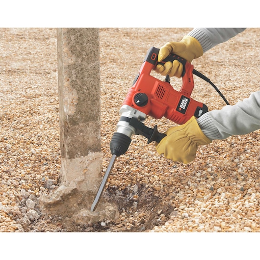 Photo of BLACK+DECKER KD1250K rotary hammer drill in use on a concrete post outdoors, gloved hands holding the tool.