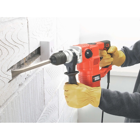 BLACKDECKER KD1250K rotary hammer in use chiseling a groove in a white brick wall, close-up view.