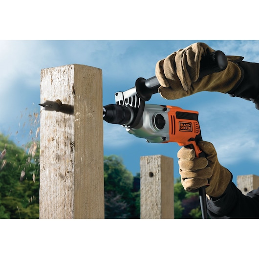 BLACKDECKER KR8542BK corded drill in use drilling through a wooden post outdoors.