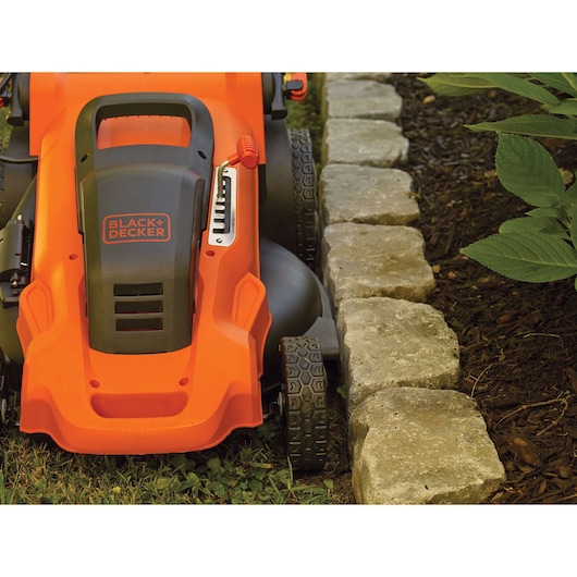 BLACK+DECKER LM2000 lawn mower close-up showing precise edge cutting near stone border and garden bed.