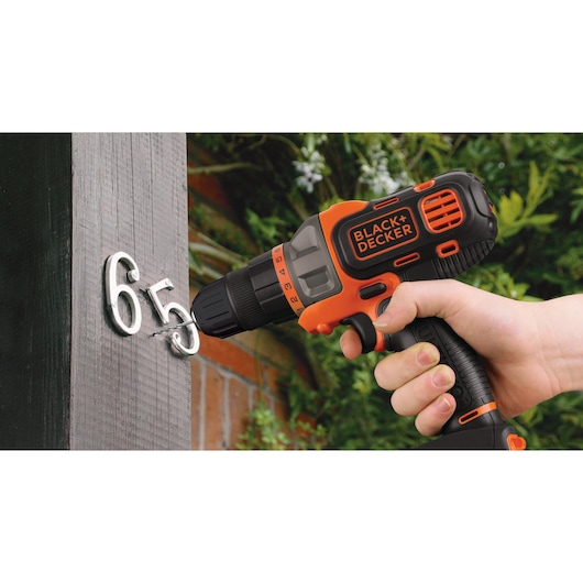 BLACK+DECKER MT218KB cordless drill used to install house numbers on a wooden post outdoors.