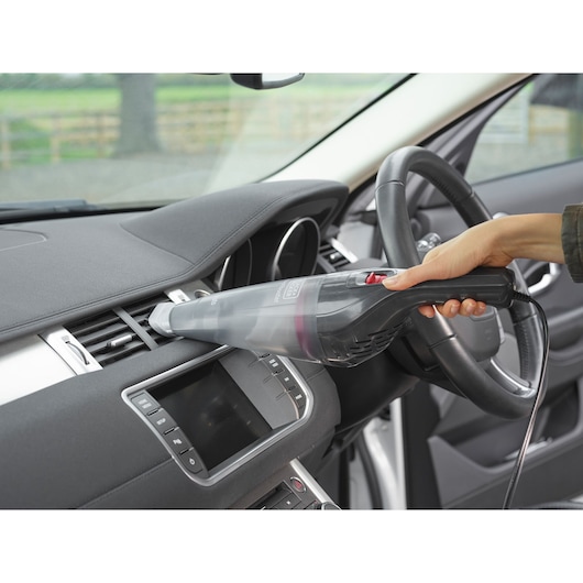 A hand using a BLACK+DECKER handheld vacuum cleaner to clean the air vents inside a car.