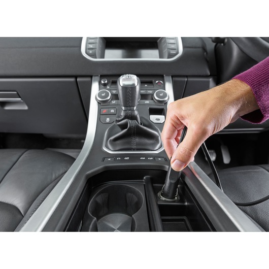 A person plugs a device into the car's cigarette lighter socket in the center console near the gear shift.