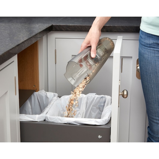 BLACKDECKER NVC115JL handheld vacuum emptied into kitchen trash bin, close-up side angle.