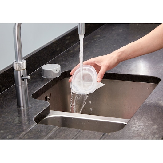 BLACKDECKER NVC115JL vacuum filter being rinsed under faucet in kitchen sink.