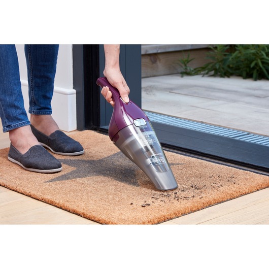 BLACK+DECKER NVC115W handheld vacuum, purple and grey, used to clean dirt on entrance mat.